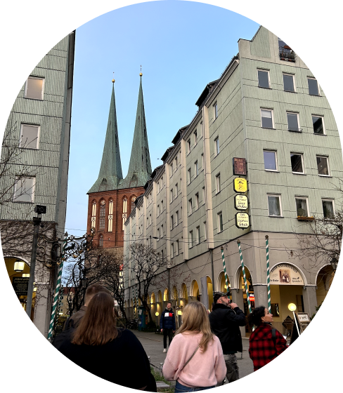 Menschen auf belebter Straße vor historischen Gebäuden und Stadtkirche mit zwei Türmen