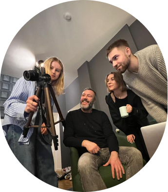 Vier Personen schauen gemeinsam auf eine Kamera auf einem Stativ in einem Raum.